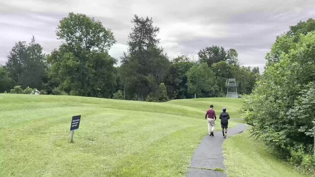 Multiracial family father and son explore Great Serpent Mound Earthworks in Peebles, Ohio. Slow motion footage shows walking path, and long serpentine curving mound making the body of the snake.