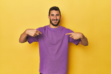 Young Hispanic man on yellow background surprised pointing with finger, smiling broadly.