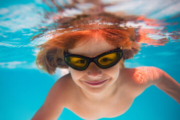 Summer child boy relax at aquapark. Summertime vacation. Little kid swim underwater in pool. Kid wearing summer goggles swims under water in poolside. Underwater photo.