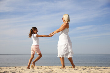 Cute little girl with grandmother spending time together on sea beach