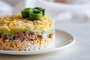 Layer canned tuna, cucumber, egg and cheese salad on white plate on a table. Selective focus. Copy space, close up