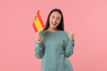 Emotional young woman holding flag of Spain on pink background
