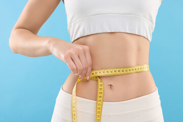 Slim woman measuring waist with tape on light blue background, closeup. Weight loss - obrazy, fototapety, plakaty