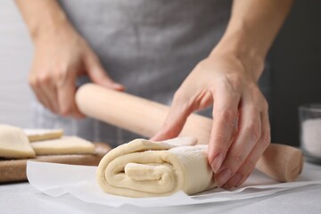 Woman with raw puff pastry dough at white table, closeup