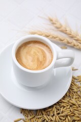 Cup of barley coffee, grains and spikes on white table, closeup