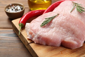 Pieces of raw pork meat, rosemary and chili peppers on wooden table, closeup