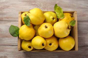 Tasty ripe quince fruits in crate on wooden table, top view