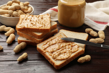 Delicious toasts with peanut butter, nuts and knife on dark wooden table