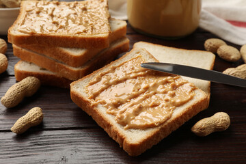 Delicious toasts with peanut butter, nuts and knife on dark wooden table, closeup