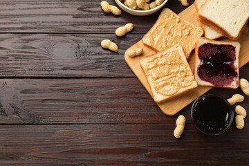 Delicious toasts with peanut butter, nuts and jam on dark wooden table, flat lay. Space for text