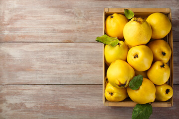 Tasty ripe quince fruits in crate on wooden table, top view. Space for text