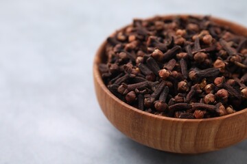 Aromatic cloves in bowl on gray table, closeup. Space for text