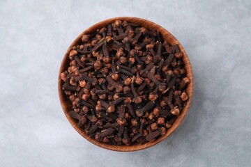 Aromatic cloves in bowl on gray table, top view