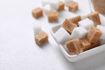 Fototapeta na wymiar Different sugar cubes in bowl on white table, closeup. Space for text
