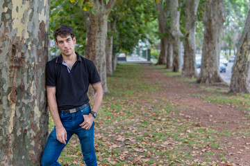 Man posing in a park leaning on a tree