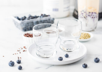 Empty glasses on a plate with ingredients to make a blueberry smoothie in behind
