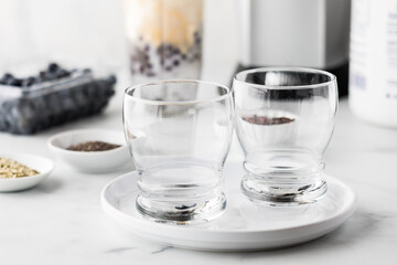 Empty glasses with Ingredients used to prepare a blueberry smoothie in behind.