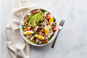 A fresh healthy tossed chicken salad with avocado and boiled egg slices.