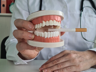 Doctor dentist holds jaw and cigarette in clinic