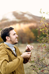 Young farmer collects rose hips from a bush against the backdrop of mountains. Side view