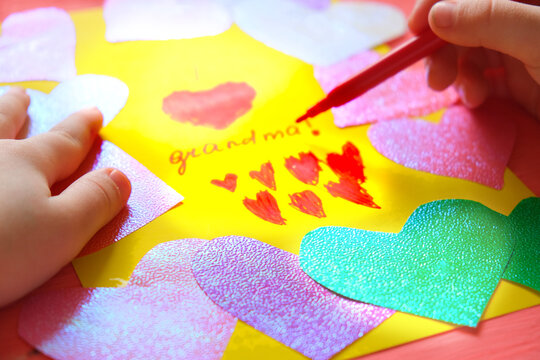 Little girl making card for grandma. Colorful pink background with paper decoration, multicolored hearts,  Handmade concept for birthday, mothers day and grandparents day