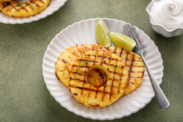 Grilled pineapple served with fresh lime wedges and whipped cream
