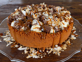 Banoffee pie decorated with chocolate chunks, whipped cream, coconut shavings and caramel drizzle