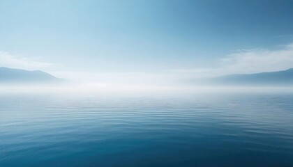 Fototapeta premium Serene seascape with a tranquil blue sea merging with a foggy sky and distant mountains.