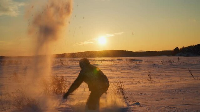 A young man cheerfully throws snow against the background of a golden sunset. A happy man throws snow into the air.