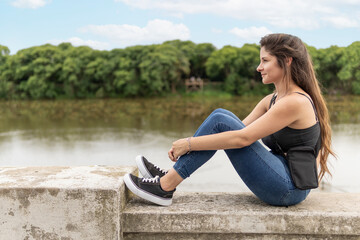 Young woman sitting on the waterfront looking at the river with a lost look