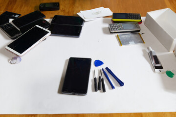 Image of a cell phone lying on a work desk with tools for repairing it.