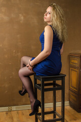 Fototapeta premium a beautiful blonde in a blue short dress and black stockings sits on a high chair.