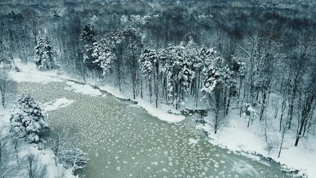 A drone flight over a frozen pond and snow covered trees in the middle of winter.