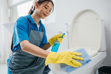 Dedicated maid in rubber gloves scrubs toilet seat with cloth ensuring hygiene in the bathroom. Her...