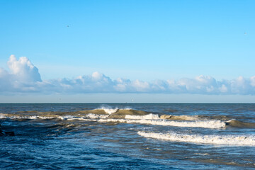 Sea surf against a background of white clouds in a blue sky