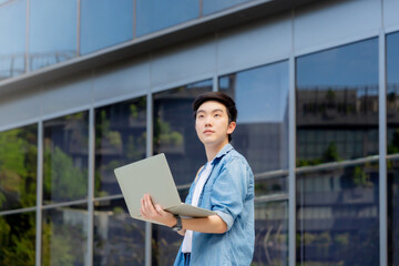 Portrait of handsome Asian student using computer laptop. A young man standing outdoor happy smiling