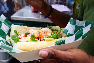 A delicious shrimp sandwich purchased at a food truck festival is just seconds from being devoured.