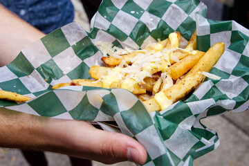 A foodie holds gourmet cheese topped French fries purchased at a food truck festival.
