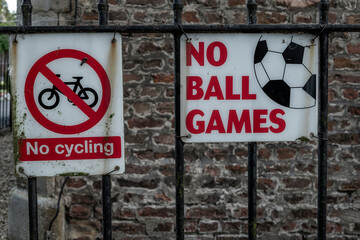 Prohibitory signs for no cycling and no ball games affixed to a fence - obrazy, fototapety, plakaty