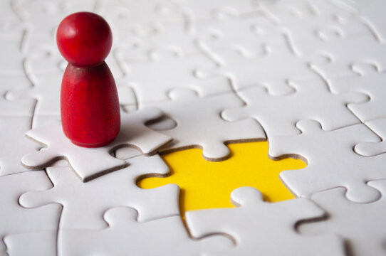 Red wooden doll on top of jigsaw with missing jigsaw puzzle. Hiring and employment concept