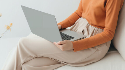 Naklejka premium Woman in a soft peach sweater using a laptop on her lap, embodying the comfort of slow living and the joy of simple technology in a serene setting