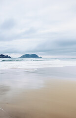 Fototapeta premium Sandy beach in nasty weather, stormy landscape. Deep blue sea under the clouds. Stunning picturesque beach with fine sand, dark gray cloudy weather and big waves. Foaming sea water with bronze sand. 