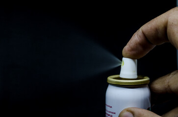Close up view of a man spraying, A spray can  in a hand on a black background
