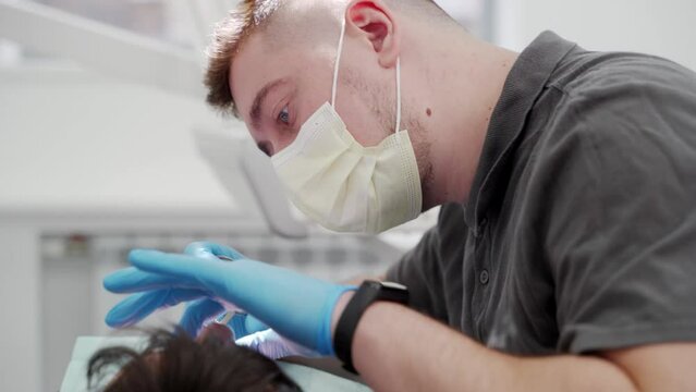 Male endodontist cleaning root canal and cauterizes dental nerve in the modern dental clinic. Concentrated dentist treating carefully patient teeth. Professional oral surgeon treating root canals.