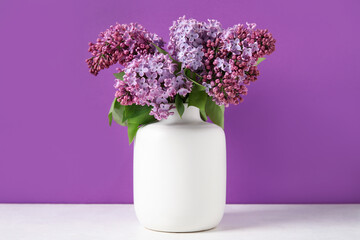 Vase with beautiful lilac flowers on light table against color background