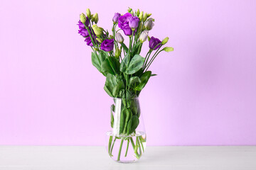 Vase with eustoma flowers on table near lilac wall