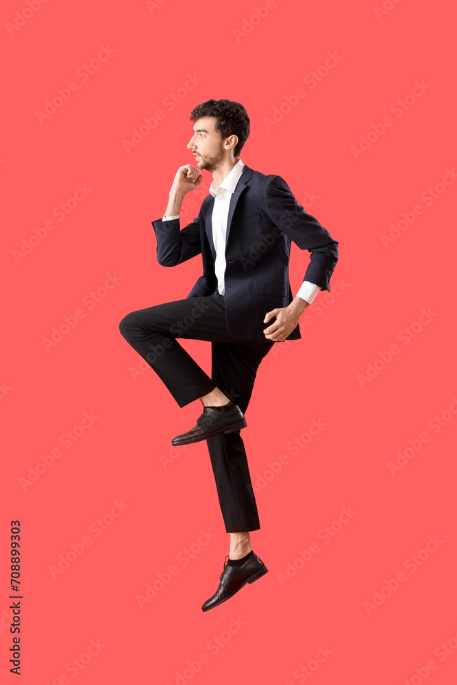 Poster Young man in suit jumping on red background