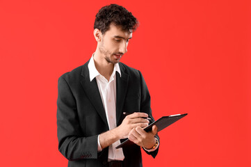 Young man in suit with clipboard on red background
