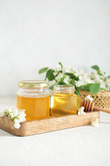 Jars of honey with flowers of acacia on light background