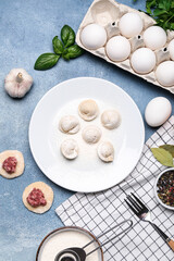 Plate with uncooked dumplings and ingredients on blue background
